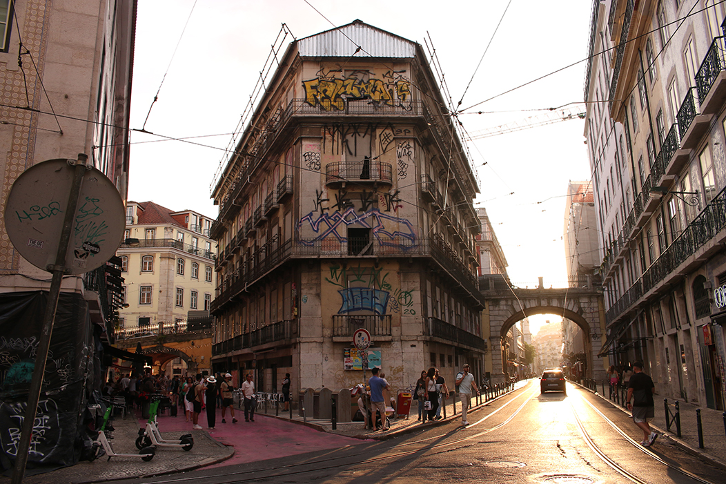 "Perspectiva", fotografía tomada en Lisboa, o 2-6-23. Mostra a bifurcación entre as rúas Nova do Carvalho (coñecida como Pink Street polo seu pavimento rosado) e S. Paulo, cunha perspectiva de dous puntos de fuga. A Rúa de S. Paulo, á dereita, reflicte os raios dourados do solpor sobre o chan húmido.